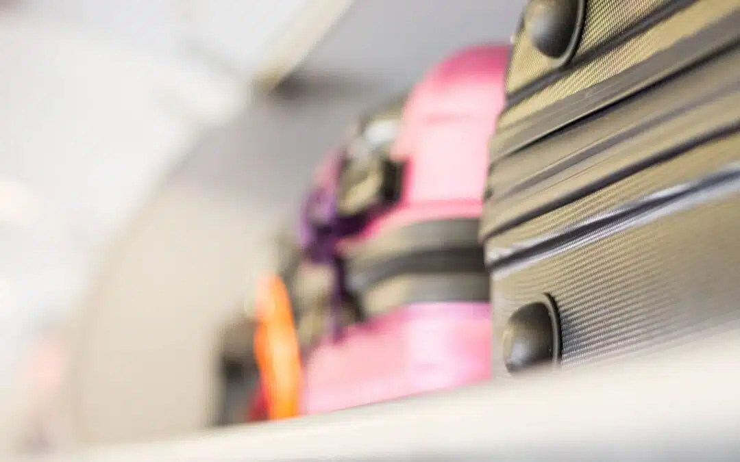Suitcases in an overhead compartment, with a focus on a pink and a black suitcase.